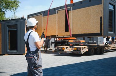 construction worker supervising loading of modular house onto truck